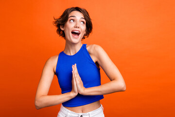 Photo of excited funky lady wear blue singlet praying looking empty space isolated orange color background