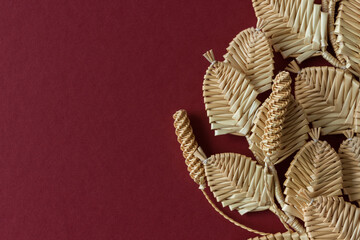 Obraz premium The branch with leaves is made of straw. Straw wall decoration. The products are made of straw. Decoration of straw on a red background