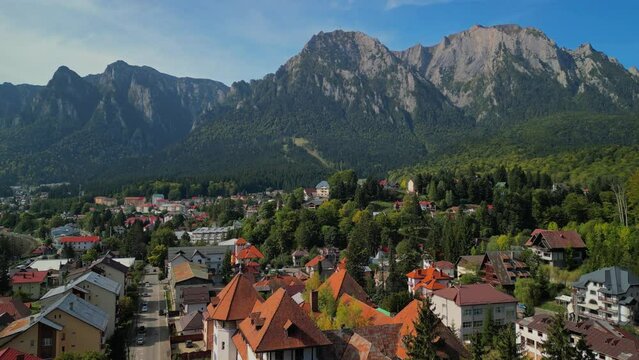 Astonishing aerial view with the rocky mountains filmed in cinematic style. Romanian landscape above Busteni city in a sunny day with blue sky