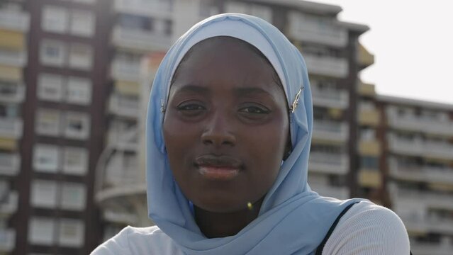 African woman with muslim hijab looking at camera smiling in the urban city