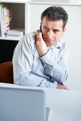 Fototapeta premium Businessman, phone and secret call in office private information, confidential or sneaky discussion. Male person, mobile or talk at laptop for inside trade, crime job or company online security break