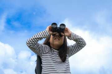 Obraz premium Cute little girl with binoculars on the mountain on a sunny day. Young girl uses binoculars when going hiking. Active young girl uses binoculars on a trip and smiles happily.