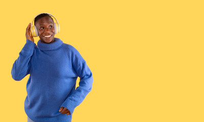 Cheerful young woman  in blue sweater posing isolated on yellow  background studio portait. People lifestyle concept. Mock up copy space. Listen music with headphones, dancing