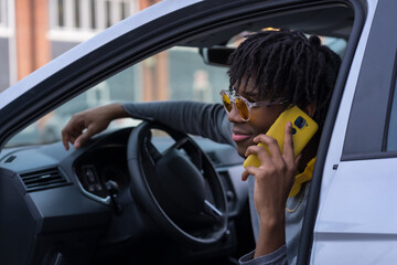Cool african young man talking to the phone into a car