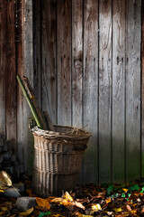 Woven basket filled with tools stands on the outer wall of a wooden hut illuminated by the sun....