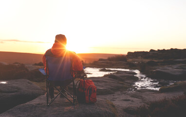 Fototapeta premium mature man hiking in mountain to take timelaps of sunrise, exercise and fitness for wellness, healthy lifestyle and smile. senior mature gentleman sitting on rock, enjoing calm day toned image