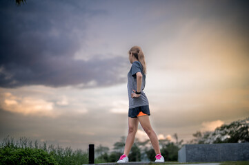 A fit young woman is engaging in warm-up exercises outdoors before her training session at the park.