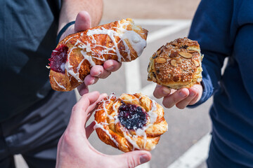 The hands of three people holding pastries in a sunlit parking lot