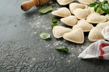 Fototapeta na wymiar Italian ravioli pasta in heart shape. Tasty raw ravioli with flour and basil on dark background. Food cooking ingredients background. Valentines or Mothers Day lunch ideas. Top view with copy space.