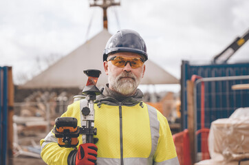 Closeup portrait of a Surveyor builder site engineer with theodolite total station at construction site outdoors during surveying work - obrazy, fototapety, plakaty