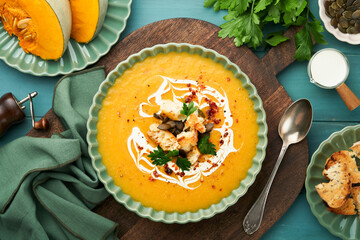 Pumpkin and carrot cream soup with herbs, seasonings and seeds in bowl on dark wooden background in rustic style. Thanksgiving traditional autumn pumpkin cream soup. Top view.