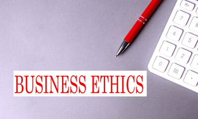 BUSINESS ETHICS text written on a gray background with pen and calculator