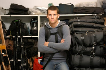 joven hombre excursionista de brazos cruzados en tienda de mochilas esperando