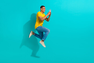 Full length profile portrait of excited handsome guy jump rush use smart phone empty space isolated on turquoise color background