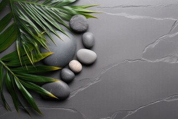 Top view of palm leaves and grey stones on a grey spa background, embodying the spa concept.