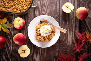 Homemade apple crumble crisp cake on white plate with autumn leaves on the wooden background