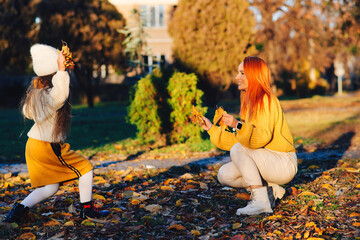 Happy little girl and her mother playing in the autumn park. Lovely family laughing on autumn walk.