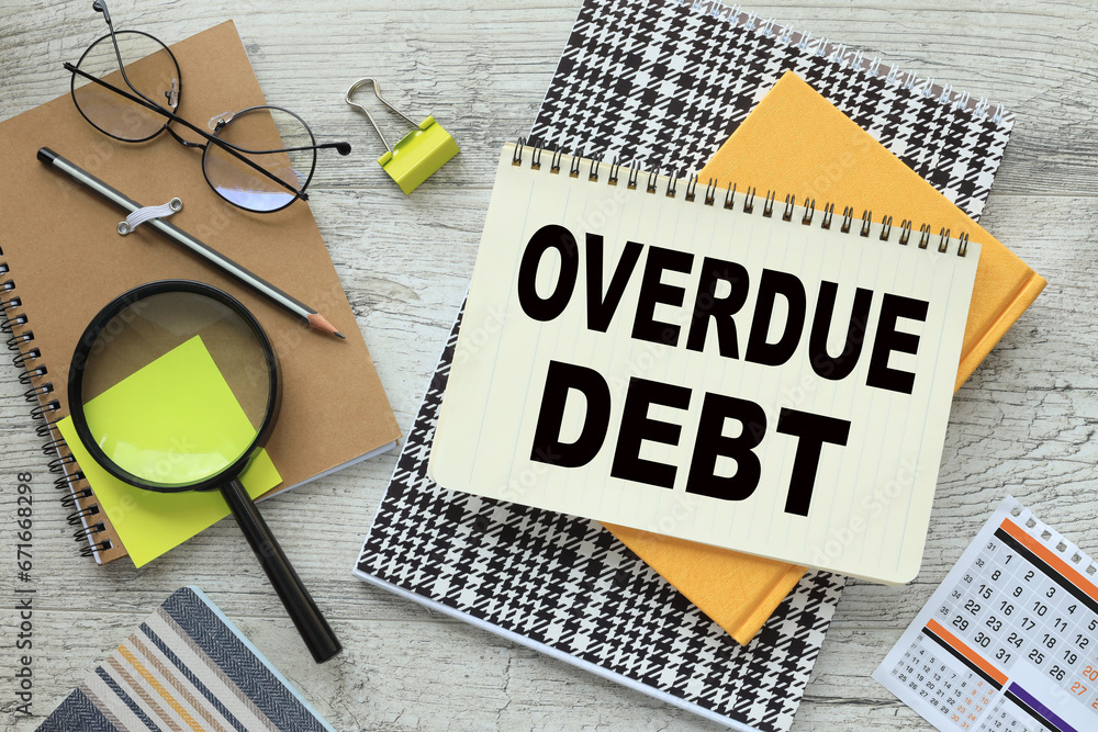 Poster overdue debt text on a notebook with a spiral in the middle of the table near glasses and a magnifyi