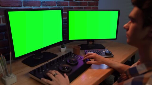 Closeup portrait of man working at the desk looking in chroma key monitors editing video settings using mixer.