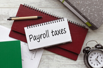payroll taxes . text on a notebook on a diary. a table clock