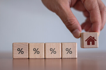 The concept of interest rates and mortgage rates Businessman's hands place wooden blocks with house icons and percentage symbols.