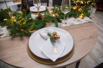 Festive table setting. Glass goblet. Christmas dinner in an interior with lights. Christmas tree with garlands and toys and balls.