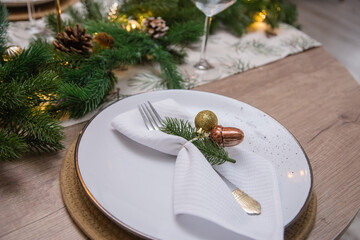 Festive table setting. Glass goblet. Christmas dinner in an interior with lights. Christmas tree with garlands and toys and balls.