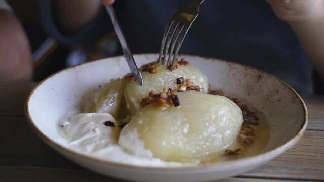 A man cuts zeppelins served in a plate with sour cream in a restaurant. Close-up