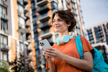 Photo of dreamy sweet girl dressed orange t-shirt eyewear backpack communicating modern gadget app...