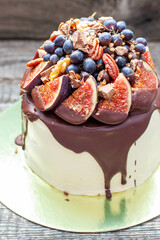 Delicious cake with figs dipped into melted chocolate, pecan nuts, grapes, chocolate bites and cookies on the top. Concept of autumn or summer cake