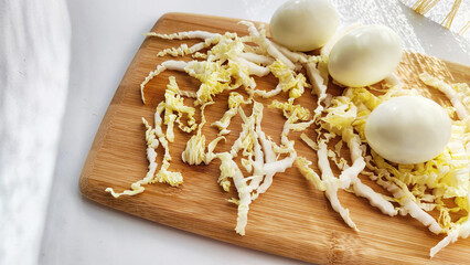 Chopped Peking cabbage and peeled eggs on cutting board as a background. Cooking a healthy eco-friendly salad from natural products. Copy space and place for text