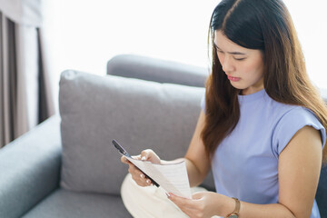 Asian woman holding paper document calculating money savings paying bills in mobile application...