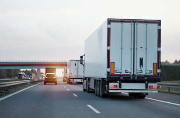 Modern white semi-trailer trucks on the highway driving in the right lane. Commercial vehicle for...