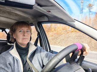 Portrait of female driver in solo journey. Adult mature woman holding steering wheel and looking through windscreen in travel by vehicle on vacation. Lady girl who is owner or rent a car for travel