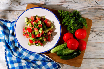 Top view of salad of cucumbers, tomatoes and parsley in a white plate with a blue border and blue on the table with checkered napkins
