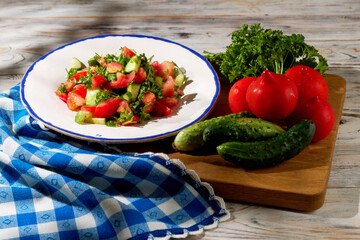 Salad of cucumbers, tomatoes and parsley in a white plate with a blue border and blue on the table with checkered napkins