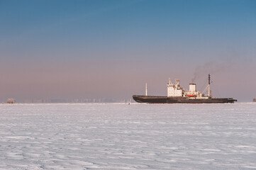 Fototapeta premium Winter shipping. Big cargo ship in frozen sea fairway