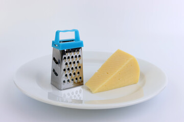 A miniature grater and a piece of cheese on a white plate.