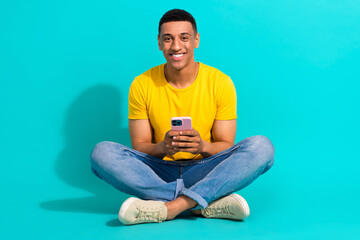 Full body portrait of cheerful man sitting floor hold use smart phone texting typing isolated on turquoise color background