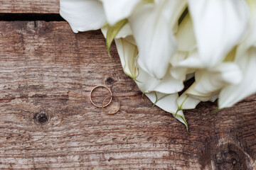 A wedding bouquet of white flowers lies on old wooden boards. Wood texture with copy space. Wedding rings.