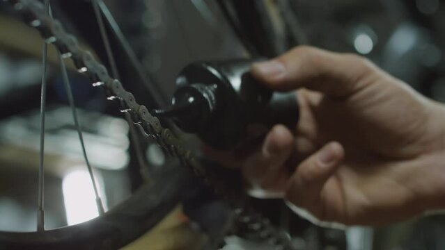 Close up shot of hand of repairman applying lubricant from bottle with nozzle to chain on bicycle