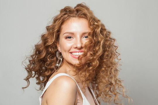 Cheerful happy woman with long natural healthy brown curly hair and cute smile looking at camera on white background. Hair care, hair treatment, wellness, joy and cosmetology concept