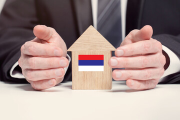 Businessman hand holding wooden home model with Serbian flag. insurance and property concepts