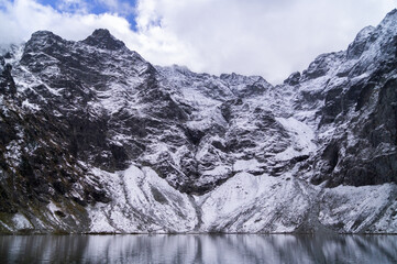 Majestic snowy peaks towering over the serene Czarny Staw lake, showcasing nature's grandeur and...