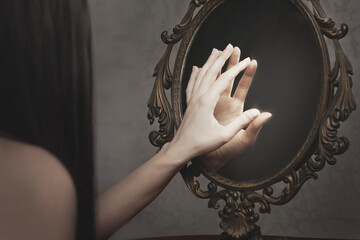 woman touches the reflection of her hand on a mirror, abstract concept