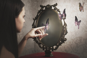 woman surprised by her exit from her mirror of surreal butterflies; ; concept of introspection and...