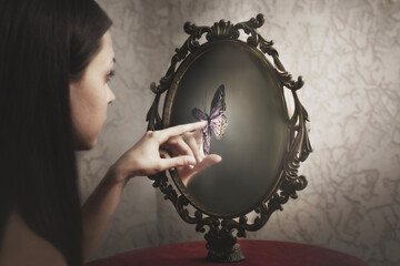 woman touches a surreal butterfly that appears in her mirror; concept of introspection and freedom