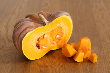 Half of an orange pumpkin next to diced pumpkin pulp on a wooden kitchen table.