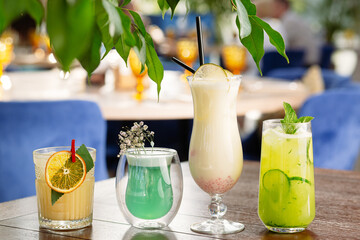 four bright non-alcoholic cocktails on the table against the backdrop of a restaurant setting,...