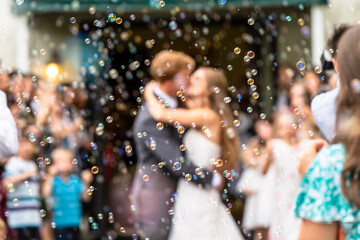 A couple kisses during their wedding exit, as seen through a sea of bubbles